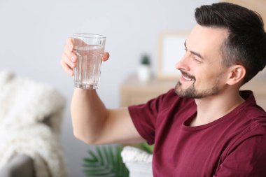 Evinde çözünmüş tabletle bir bardak suyun içinde duran genç adam, yakın plan.