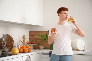 Mutfakta bir bardak portakal suyu ve çöreğiyle genç kızıl saçlı adam.