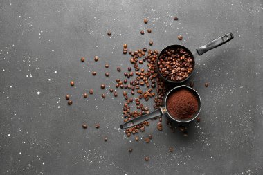 Fincanları öğütülmüş kahve ve siyah grunge arka planda fasulye ile ölçmek