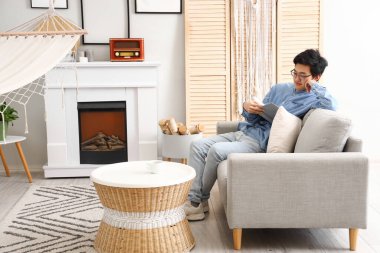 Genç Asyalı adam izin gününde evde kitap okuyor.