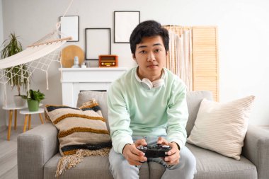 Genç Asyalı adam izin gününde evde video oyunu oynuyor.