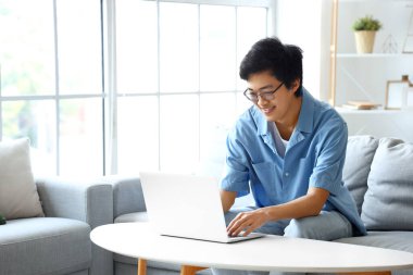 Genç Asyalı adam izin gününde dizüstü bilgisayar kullanıyor.