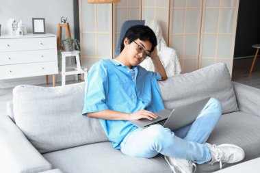 Genç Asyalı adam izin gününde dizüstü bilgisayar kullanıyor.