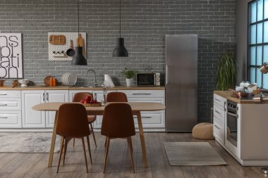 Beyaz tezgahları, yemek masası ve buzdolabı olan modern mutfağın içi.