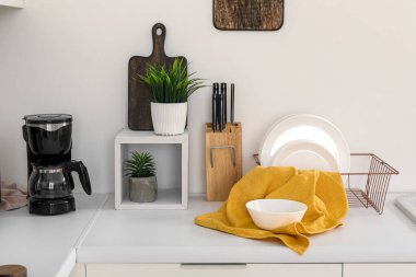 Beyaz mutfak tezgahları, kahve makinesi, tabak rafı ve mutfak aletleri.