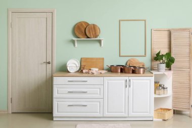 Modern mutfağın içinde beyaz tezgahlar, raflarda kesme tahtaları ve pişirme kapları var.