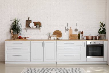 Modern mutfakta kesme tahtaları, çatal bıçakları, ev bitkisi ve elektrikli sobası olan beyaz tezgah.