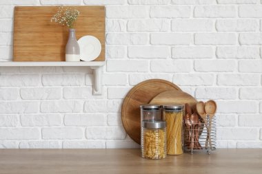 Tahta tezgah, beyaz tuğla duvarın yanında kesme tahtaları ve aletleri var.