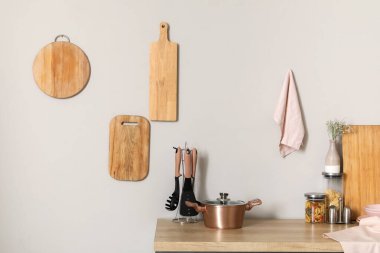 Ahşap mutfak tezgahı, yemek tenceresi, mutfak aletleri ve beyaz duvarda asılı tahta kesme tahtaları.