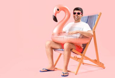 Yüzme yüzüklü genç adam pembe arka planda iskemlede oturuyor.