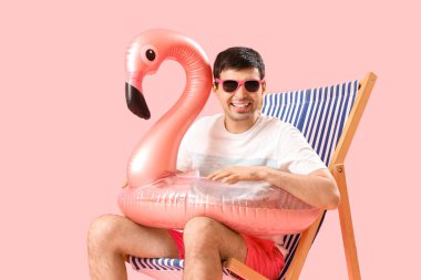 Yüzme yüzüklü genç adam pembe arka planda iskemlede oturuyor.