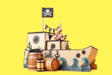Sarı arka planda oyuncak ayı ve varilleri olan korsan karton gemi.