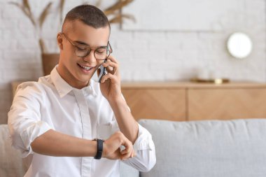 Cep telefonlu genç adam odada kol saatine bakıyor.