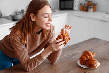 Mutfakta lezzetli kruvasanları olan güzel, mutlu genç bir kadın.