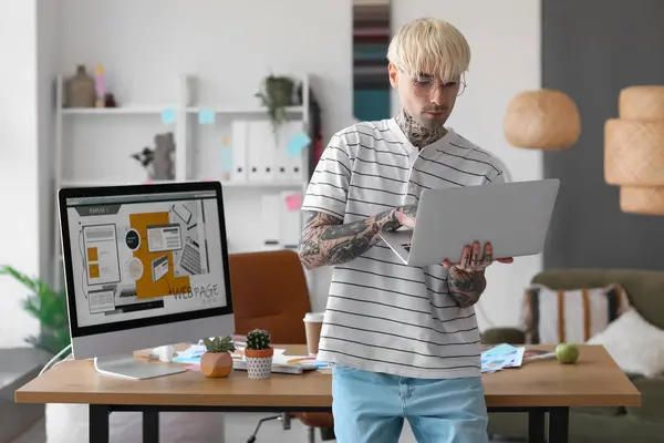 Tattooed graphic designer working with laptop in office