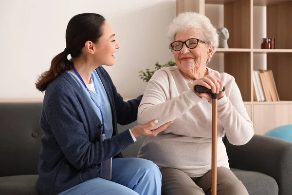 Senior woman with stick and caregiver at home