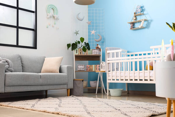 Interior of stylish bedroom with baby crib, sofa and shelving unit
