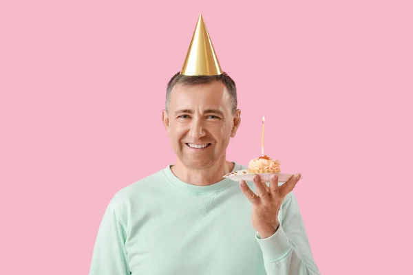Mature man with birthday tartlet on pink background