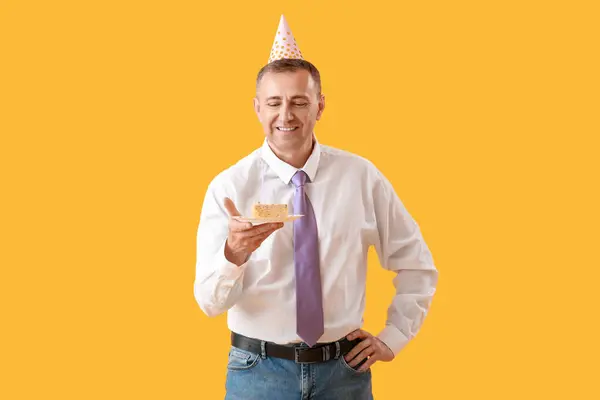 Mature man with piece of birthday cake on yellow background