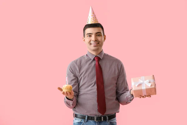 Young man with birthday cake and gift on pink background