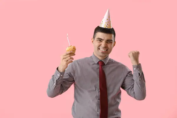 Happy young man with birthday cake on pink background