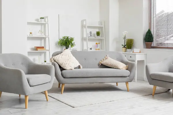 Interior of light living room with cozy grey sofa and armchairs