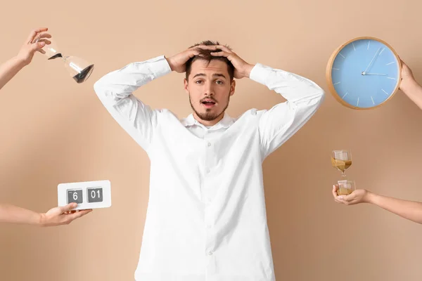 Stressed young man and hands with clocks on beige background. Deadline concept