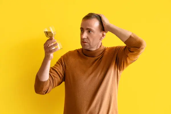 Stressed mature man with hourglass on yellow background. Deadline concept