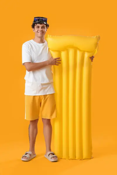Young man with swim mattress on yellow background