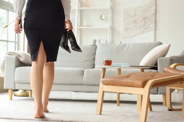 Young businesswoman with taken shoes at home after long working day
