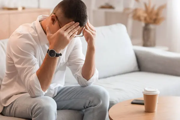 Stressed young man with wristwatch at home