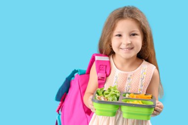 Sırt çantası ve mavi arka planda beslenme çantası olan mutlu küçük kız.