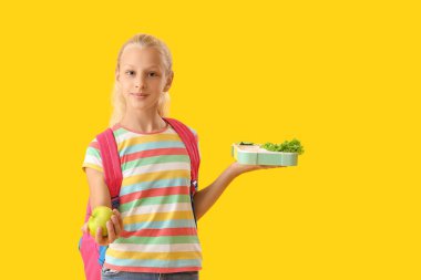 Sırt çantalı mutlu kız, beslenme çantası ve sarı arka planda taze elma.