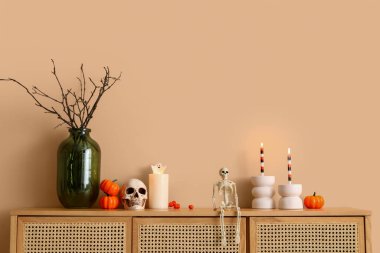 Odadaki bej duvarın yanında yanan mumlar ve Cadılar Bayramı dekoru olan çekmeceler.