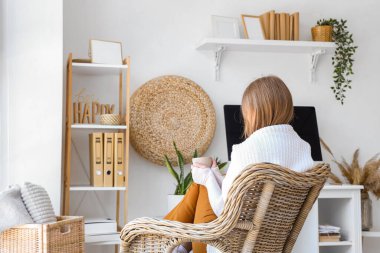 Elinde bir fincan kahve olan genç bir kadın ofisinde oturuyor.