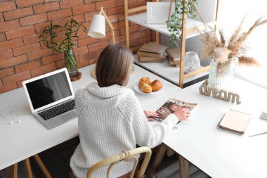 Dergisi olan genç bir kadın ofiste, arka planda oturuyor.