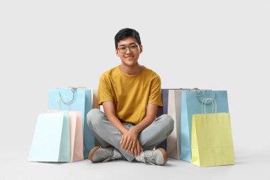 Beyaz arka planda oturan alışveriş çantalı genç Asyalı adam.