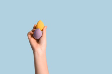 Mavi arka planda makyaj süngeri olan kadın eli