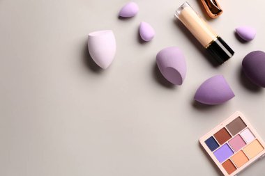 Gri arka planda farklı makyaj süngerleri ve kozmetik ürünleri olan kompozisyon