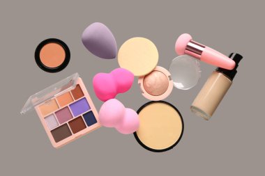 Gri arka planda uçan makyaj süngerleri ve kozmetik ürünleri