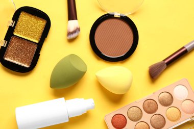 Sarı arka planda makyaj aksesuarları ve dekoratif kozmetik ürünleri olan kompozisyon