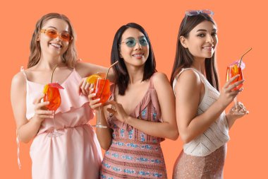 Turuncu arka planda lezzetli aperol spreyli kokteyl bardakları olan güzel genç kadınlar.