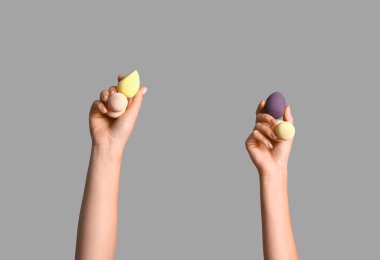 Gri arka planda farklı makyaj süngerleri olan kadın elleri