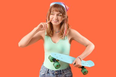 Turuncu arka planda kaykayı olan düşünceli genç bir kadın.