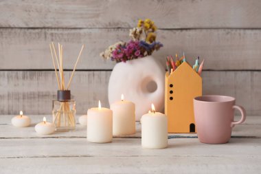 Yanan mumlar, sazlık ayırıcı, çiçekli vazo ve beyaz ahşap arka planda bir fincan çay.