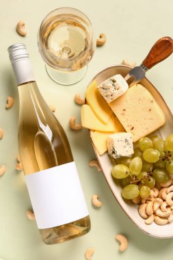 Yeşil arka planda lezzetli peynir, fındık, üzüm, şişe ve şarap tabağı.