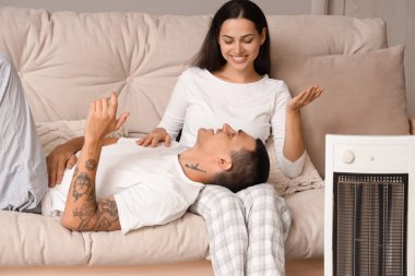 Evde elektrikli ısıtıcının yanında ısınan genç bir çift.