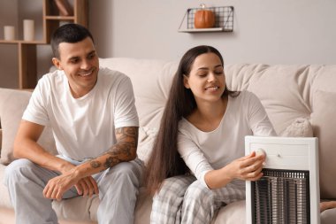 Evde elektrikli ısıtıcının yanında ısınan genç bir çift.