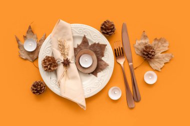 Kurumuş yapraklar, koniler ve turuncu arka planda yanan mumlarla sonbahar masası.