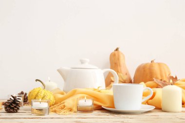 Bir fincan çay, eşarp, kozalak, balkabağı ve sonbahar yapraklarıyla yanan mumlar beyaz arka planda